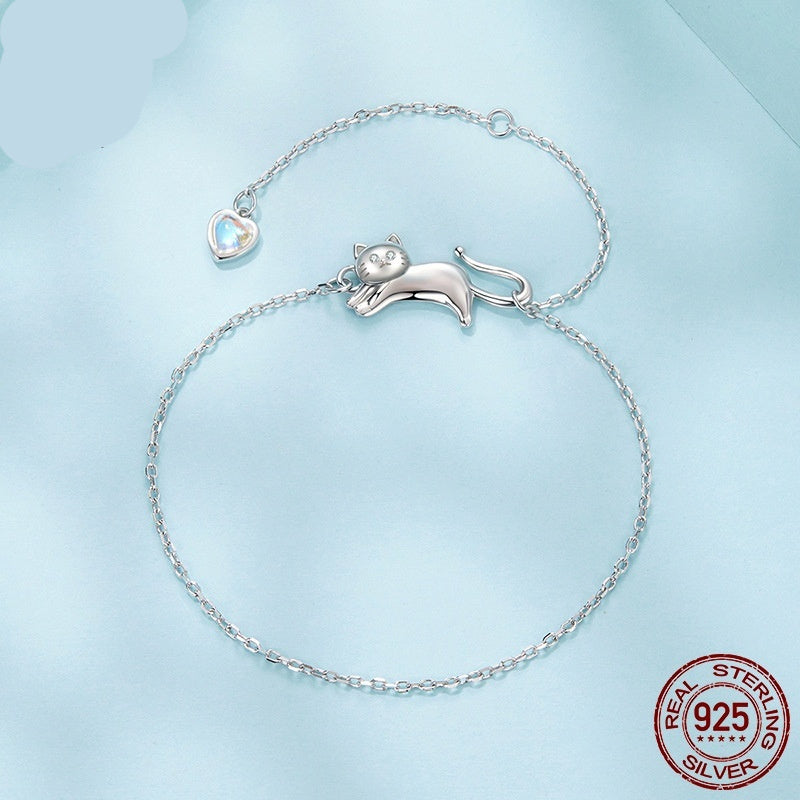 Silver chain bracelet featuring a cute cat-shaped charm and a small heart-shaped pendant on a light blue background.