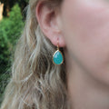 Teardrop-shaped gold earring with a turquoise stone, shown being worn to demonstrate size and fit.
