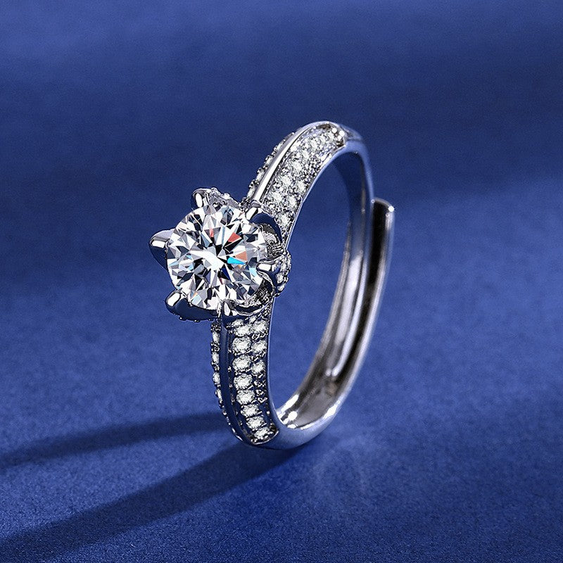 Silver pear-shaped ring with a double halo of sparkling crystals and a crystal-embellished band on a blue background.