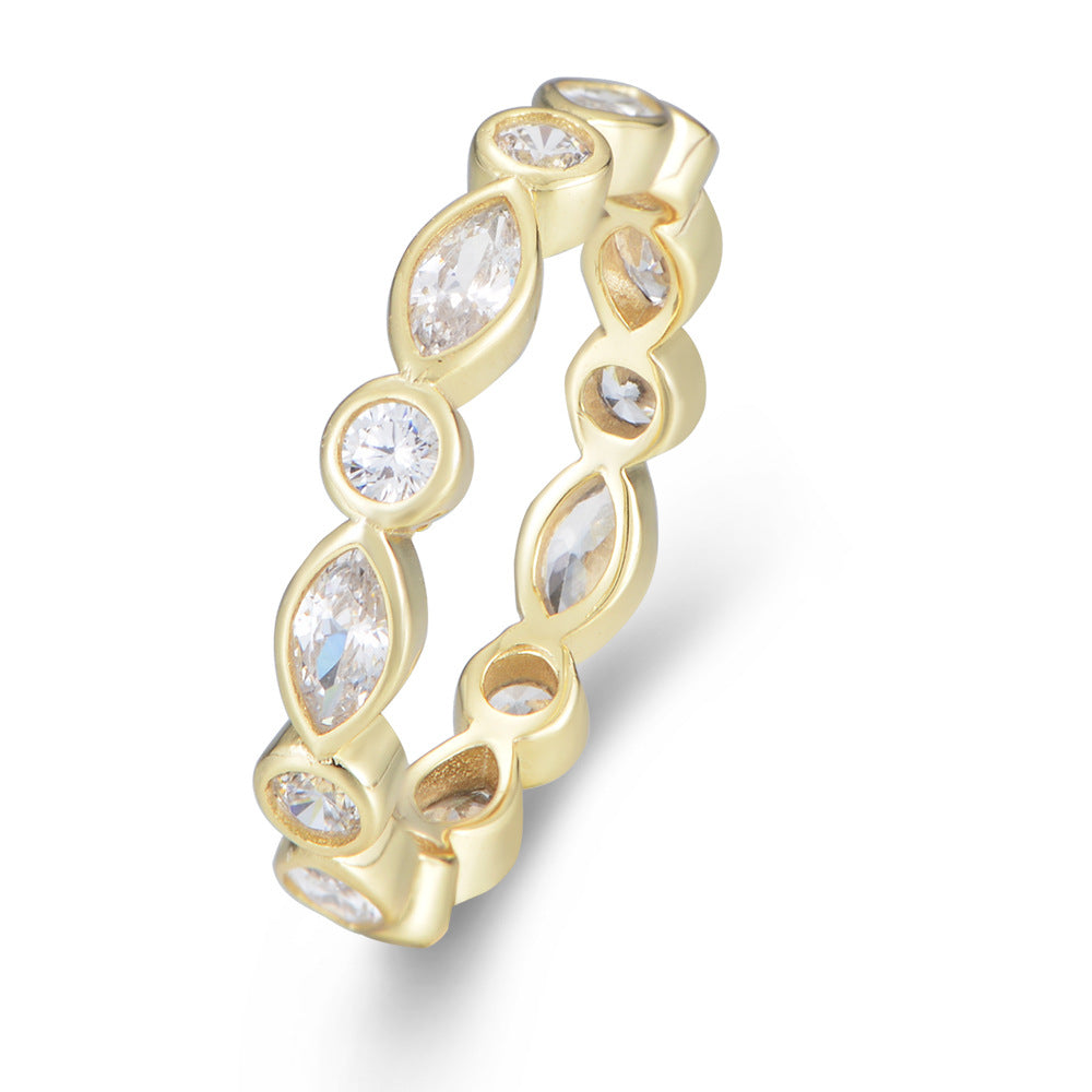 Angled view of a gold eternity ring with alternating marquise and round crystals in a bezel setting on a white background.
