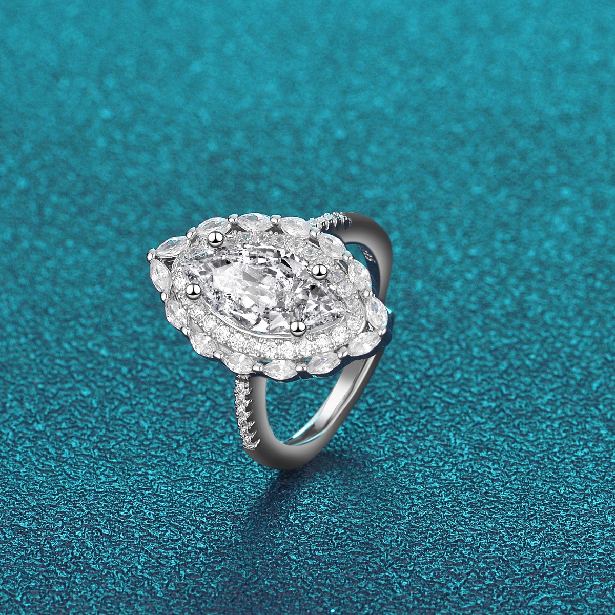 Silver marquise-shaped halo ring featuring a large center crystal surrounded by a double border of smaller stones on a shimmering teal background.
