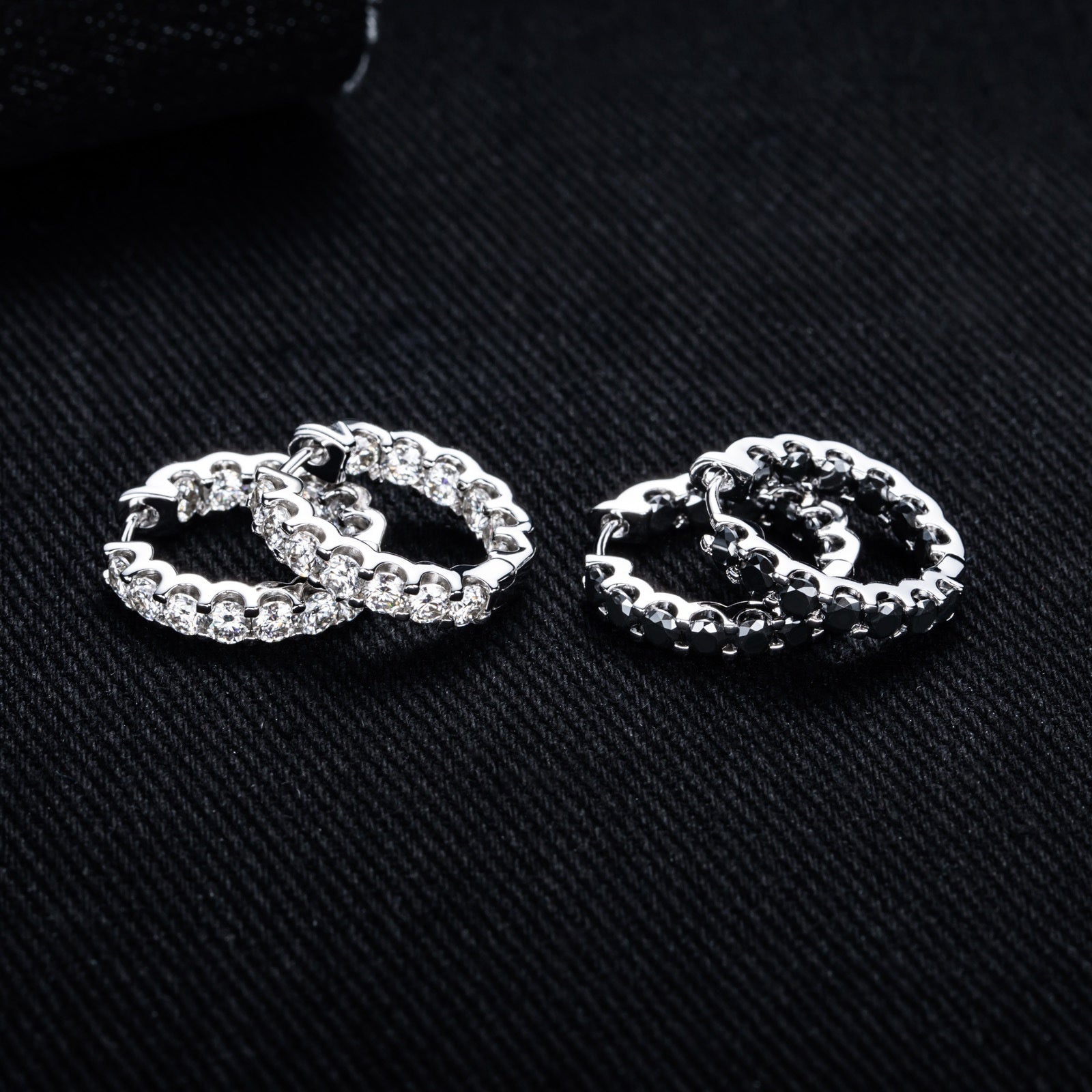 Silver hoop earrings with round-cut crystals displayed on a dark, textured black surface.