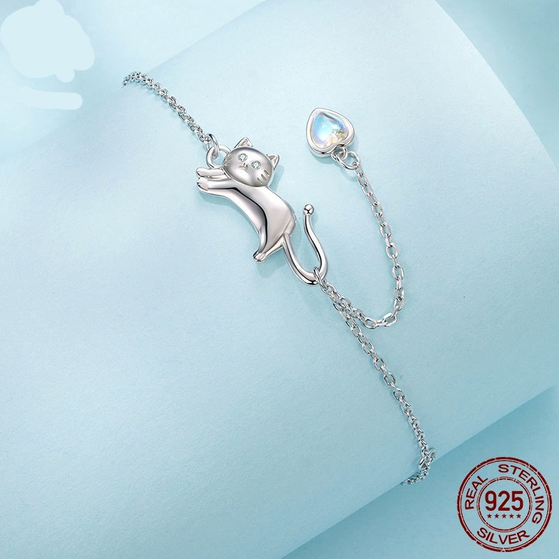 Silver chain bracelet featuring a cute cat-shaped charm and a small heart-shaped pendant on a light blue background.