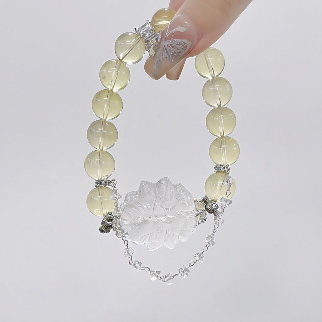 Yellow beaded bracelet with a large clear carved floral centerpiece and a delicate silver chain detail, held against a white background.