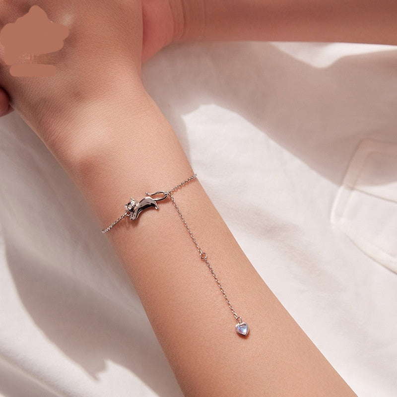 Silver chain bracelet with a cute cat-shaped charm and a dangling heart pendant, shown worn on a wrist.