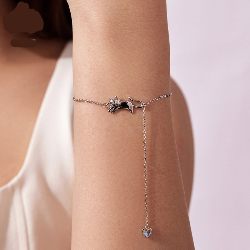 Silver chain bracelet with a cute cat-shaped charm and a dangling heart pendant, shown worn on a wrist.