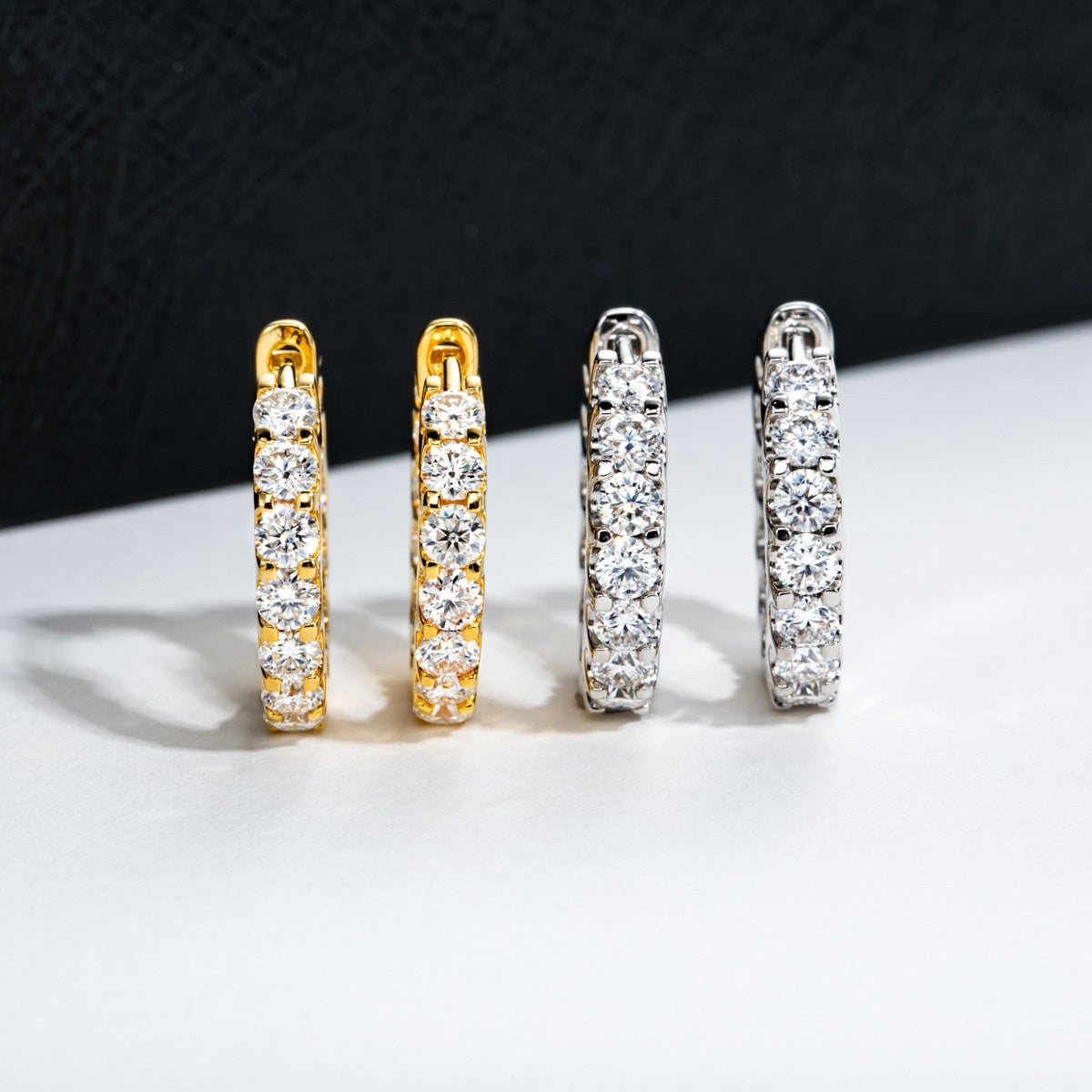Two pairs of small hoop earrings, one in gold and one in silver, both lined with sparkling round-cut crystals.