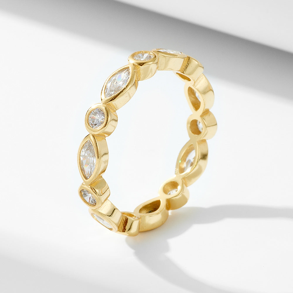 Gold eternity ring featuring alternating marquise and round-cut crystals in a bezel setting, displayed on a white surface.