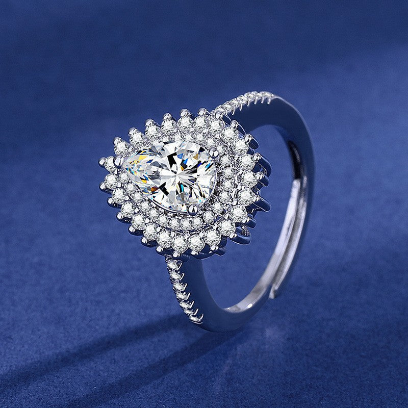 Silver pear-shaped ring with a double halo of sparkling crystals and a crystal-embellished band on a blue background.