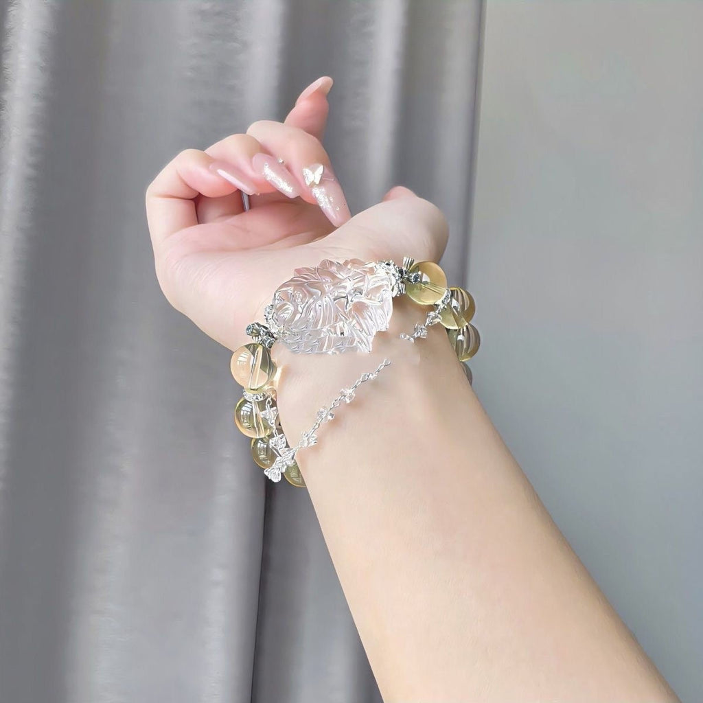 Hand wearing a yellow beaded bracelet with a large clear floral centerpiece, paired with a delicate silver chain bracelet.