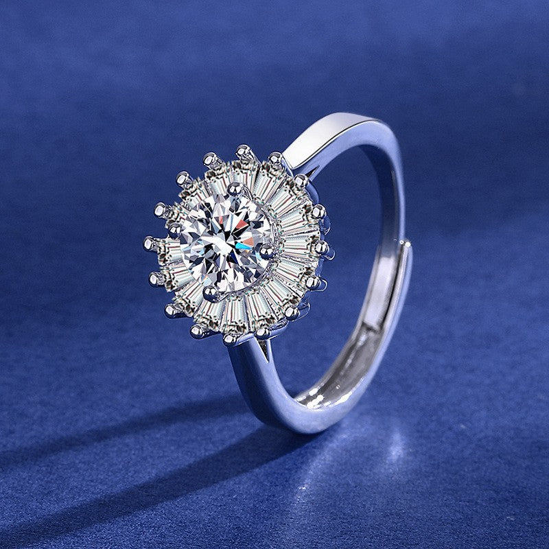 Silver sunburst halo ring with a round center crystal surrounded by tapered baguette-cut stones on a blue background.