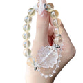 Hand holding a yellow beaded bracelet with a large clear carved floral centerpiece and a delicate silver chain with crystal accents.