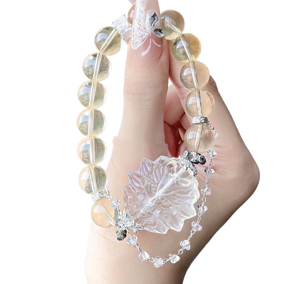Hand holding a yellow beaded bracelet with a large clear carved floral centerpiece and a delicate silver chain with crystal accents.