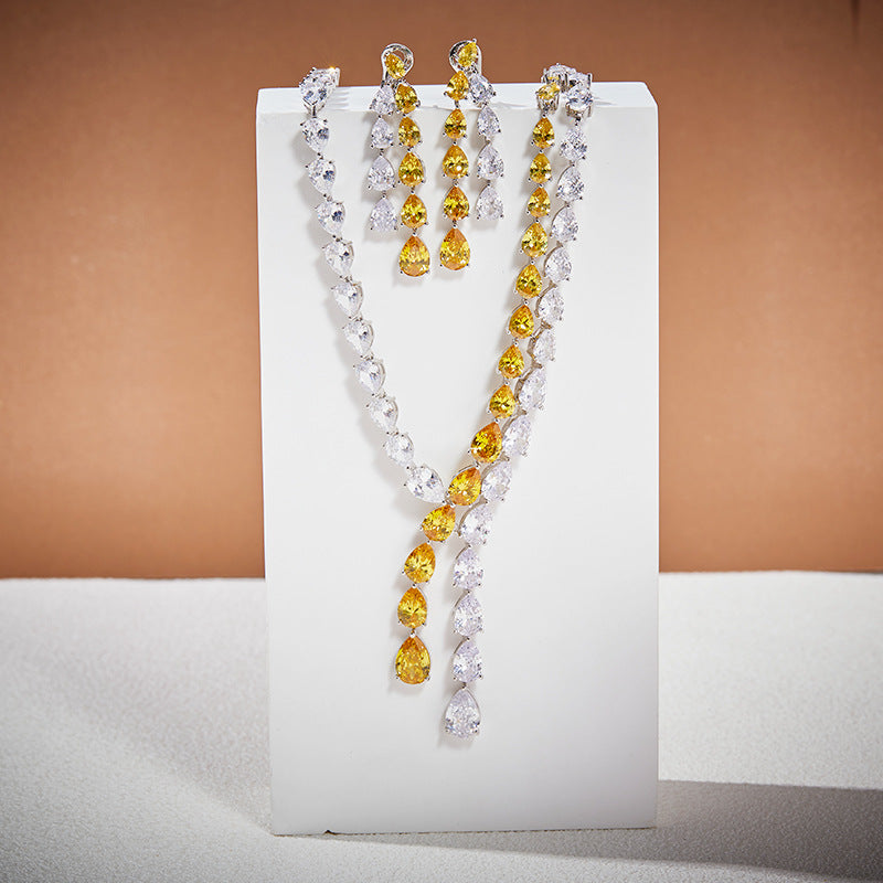 Matching jewelry set featuring long chandelier earrings and a teardrop-shaped necklace with yellow and white crystals, displayed on a white stand.