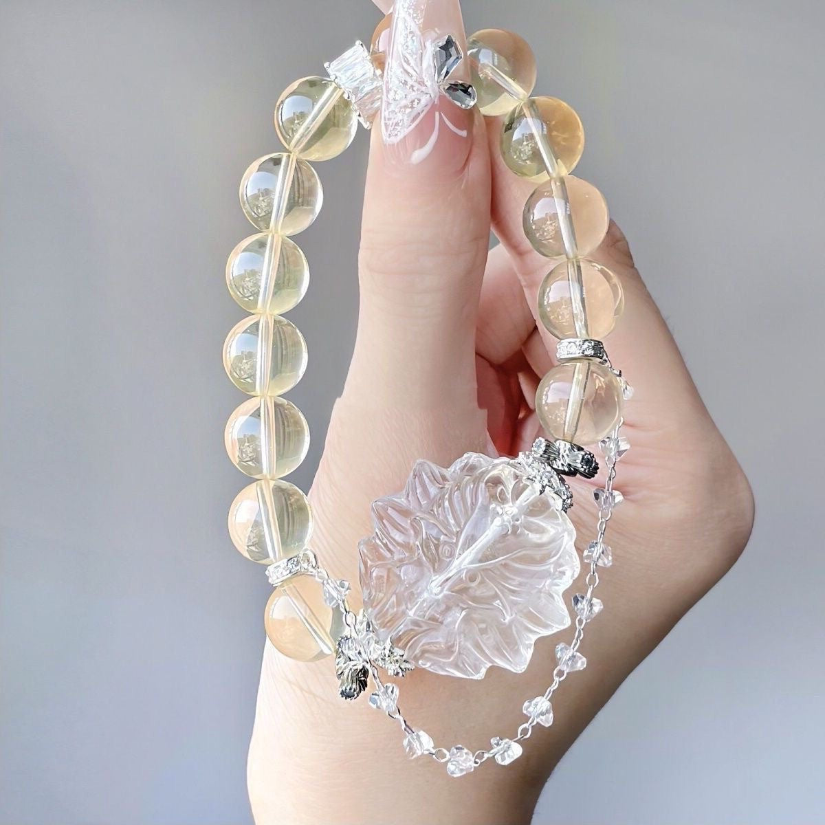 Hand holding a yellow beaded bracelet with a large clear carved floral centerpiece and a delicate silver chain with crystal accents.