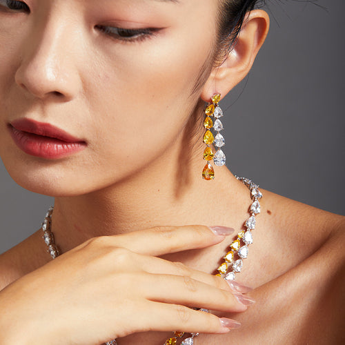 A model wearing long yellow and white crystal chandelier earrings with a matching teardrop necklace.